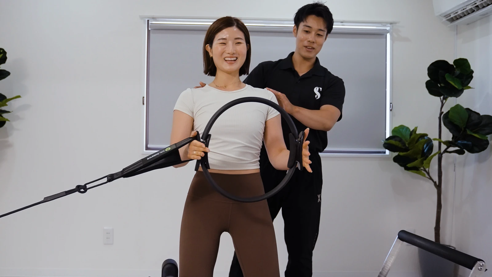 男性トレーナーがリングを使う利用者の肩と腕の動きをサポートする様子