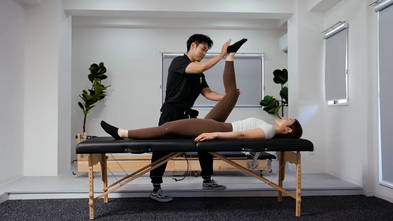 男性トレーナーがベッドに仰向けの利用者の脚を支え、脚の裏側を伸ばす様子